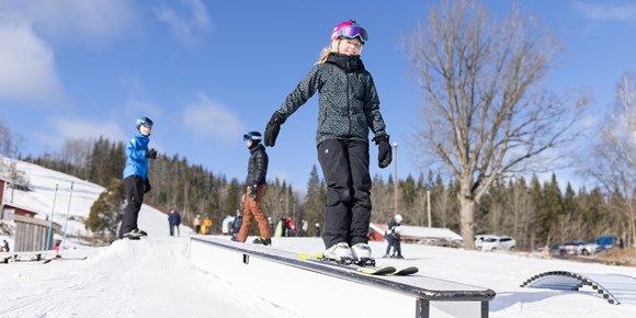 Barn åker skidor i hemmabackens snöpark tillsammans med ledare