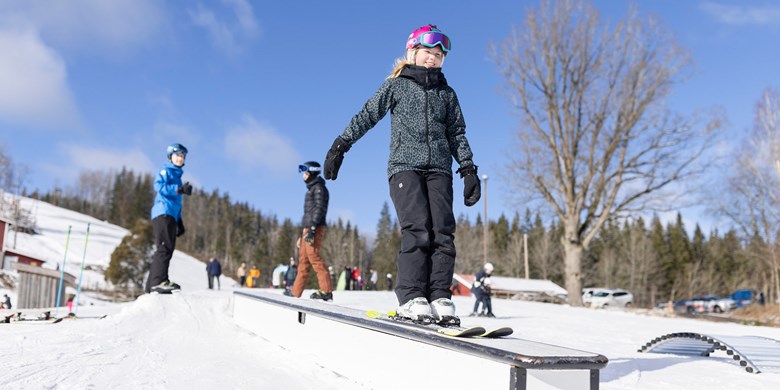 Barn åker skidor i hemmabackens snöpark tillsammans med ledare