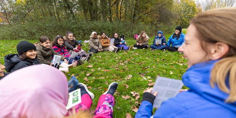 Barn i grundskola sitter i ring utomhus med sin lärare