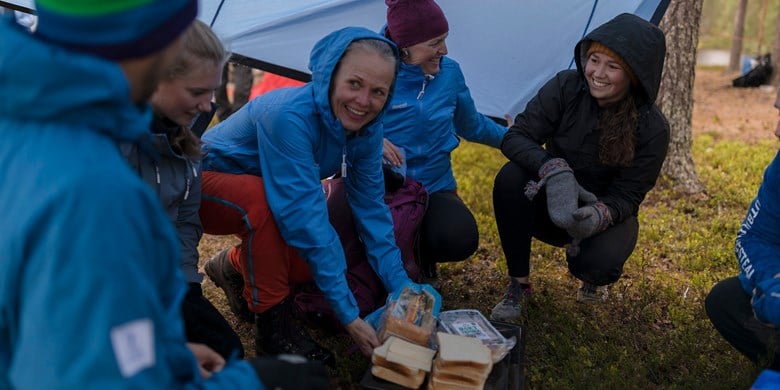 En grupp sitter under en tarp med ett fat med bröd och pålägg