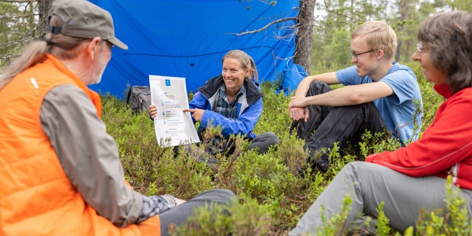 Personer sitter under vindskydd och  tittar på affisch med Krisvis-information
