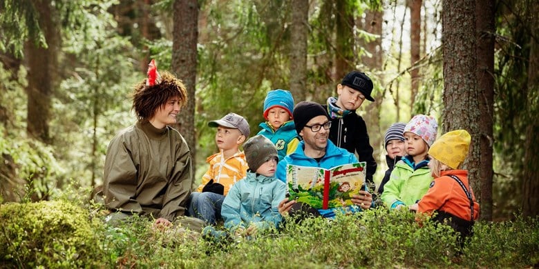 En grupp barn läser bok tillsammans med Skogsmulle och en ledare