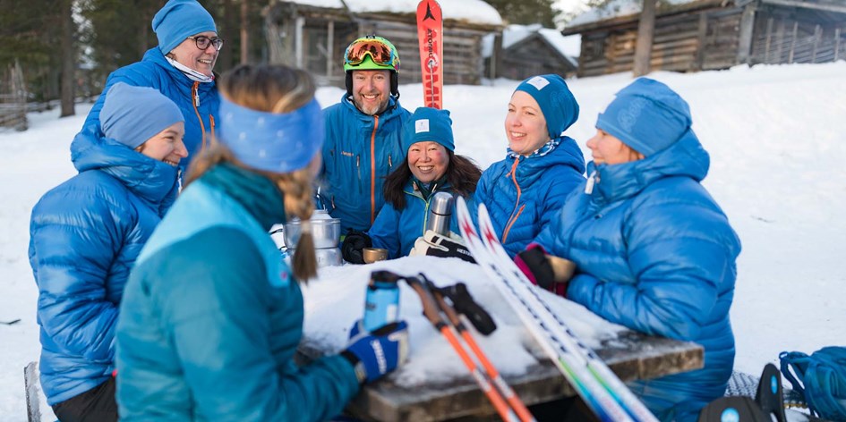 En grupp ledare fikar utomhus vid ett bord  med längdskidutrustning bredvid