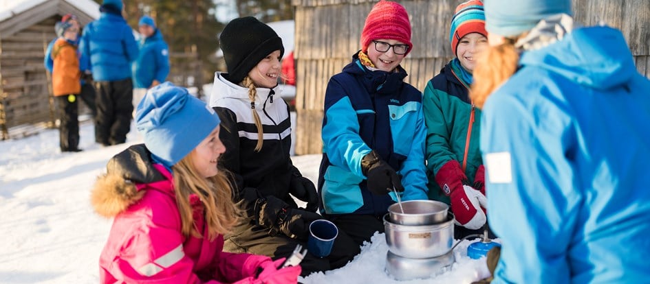 Barn och ledare värmer saft på gasolkök utomhus i snön