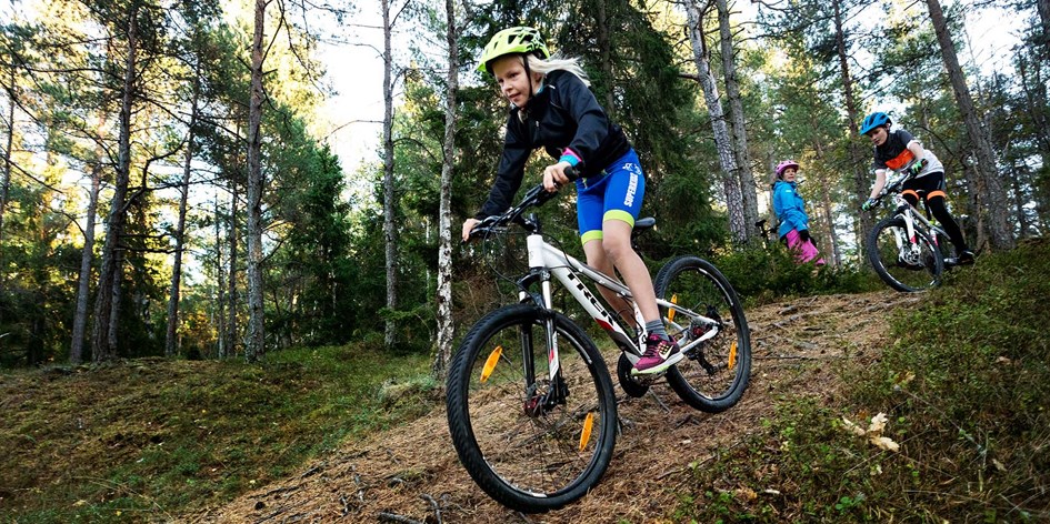 Barn cyklar mountainbike i skogen med ledare i närheten