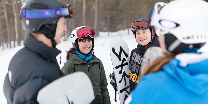Personer med snowboards står i skidbacke och pratar med en ledare