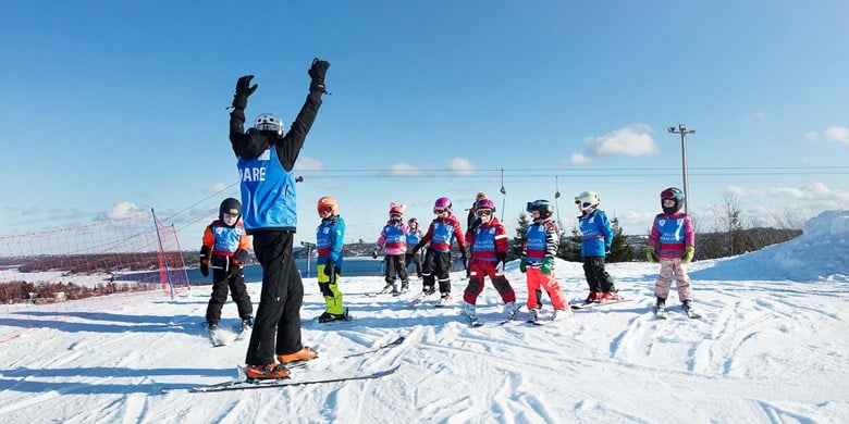Ledare i alpin skidåkning står i skidbacke tillsammans med en grupp barn