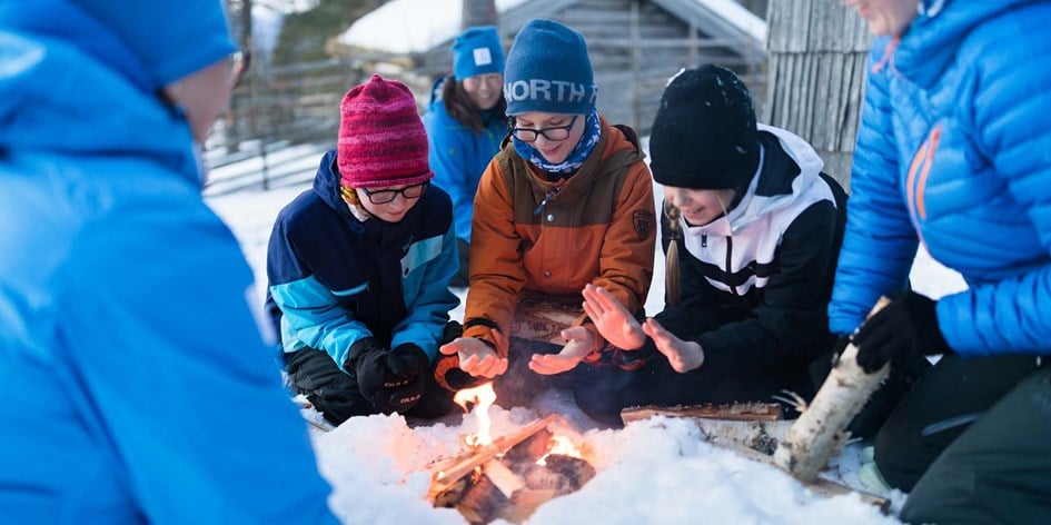 Barn och ledare sitter runt en brasa i snön